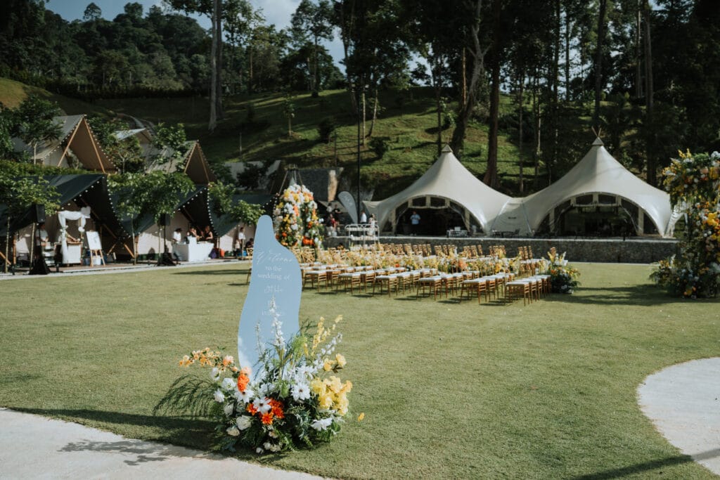 Wide view of IKAN Glampsite’s glamping wedding venue in Bentong, featuring luxury tents, event pavilion, and floral-decorated lawn in forested hillside setting.