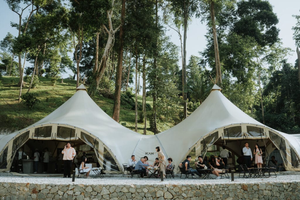 Outdoor wedding guests relaxing under spacious luxury glamping tents amidst lush forest at a garden wedding venue in Malaysia