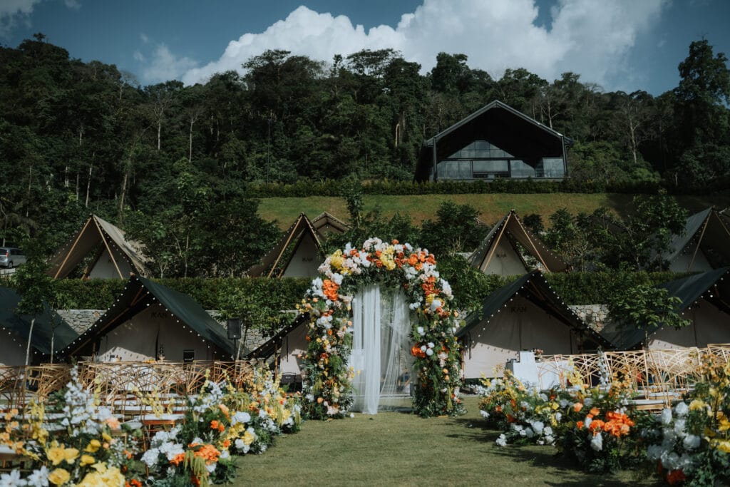 A floral wedding arch set against rows of glamping tents and a forested hillside at IKAN Glampsite, showcasing the venue’s natural outdoor landscape.
