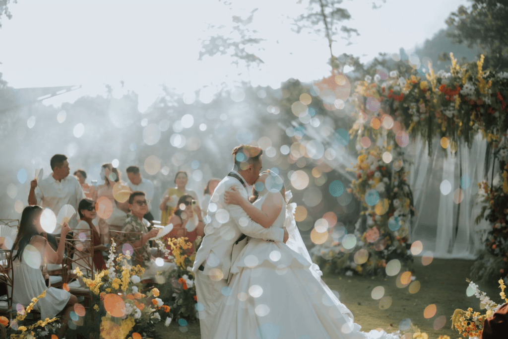 Bride and groom embracing at an outdoor garden wedding with natural light and floral arch backdrop.
