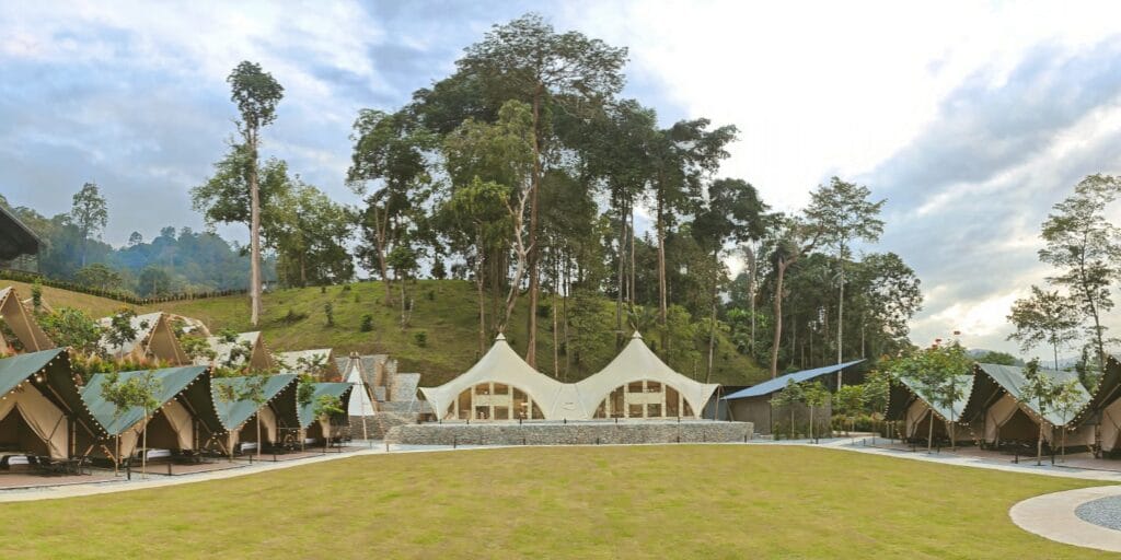 Yoga retreat glamping venue with open lawn, pavilion tents and rainforest hills in the background in Janda Baik.