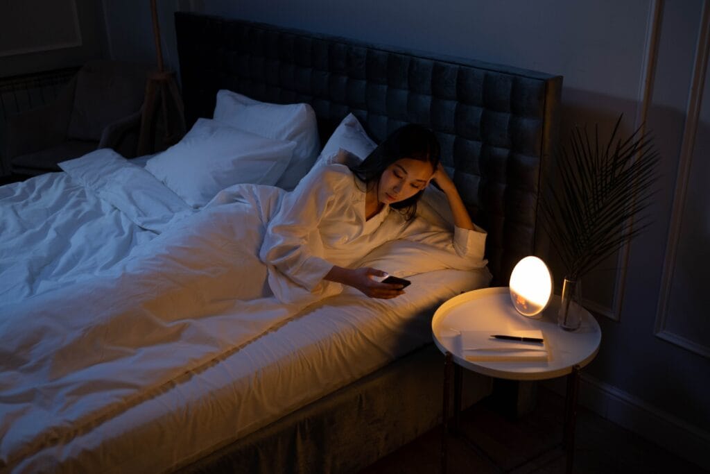Woman using a smartphone in bed at night, illustrating how screen time can negatively affect sleep quality.